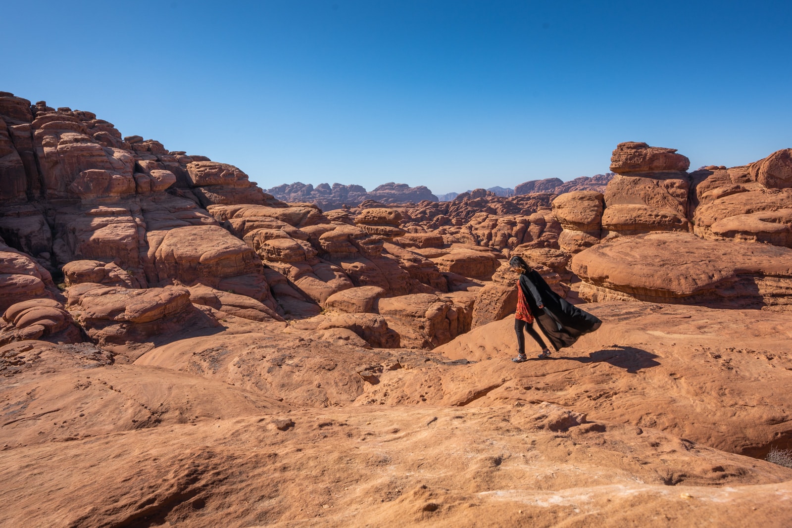 Female traveler in abaya running on rocks in Saudi Arabia