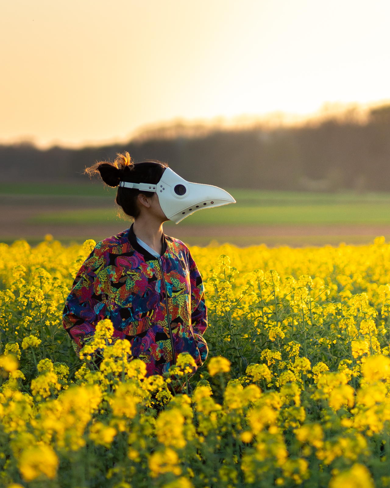 Alex in a white plague doctor mask standing in a field of flowers