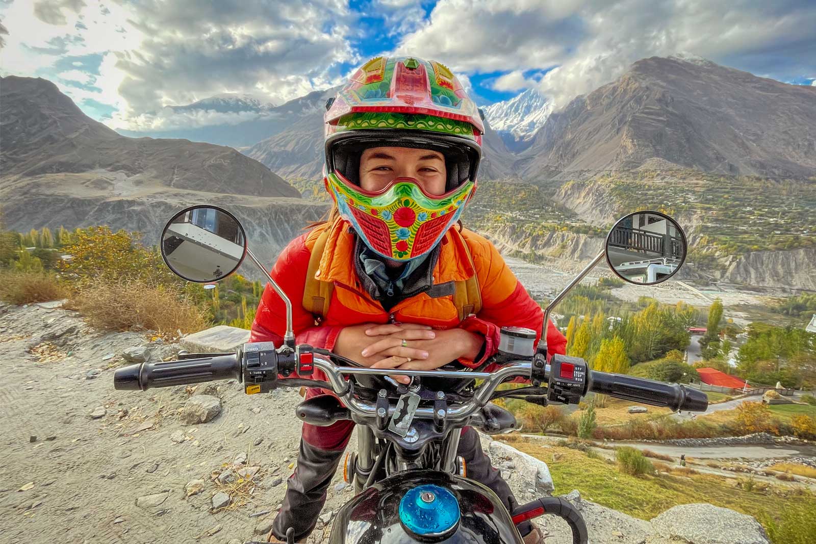 Happy female traveler and guest on a Pakistan motorcycle tour with a truck art helmet